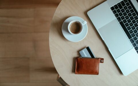 High-angle shot of a coffee cup, credit card wallet, and laptop on a wooden table.