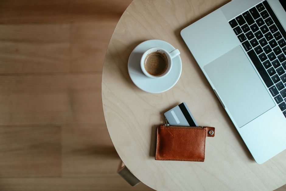 High-angle shot of a coffee cup, credit card wallet, and laptop on a wooden table.