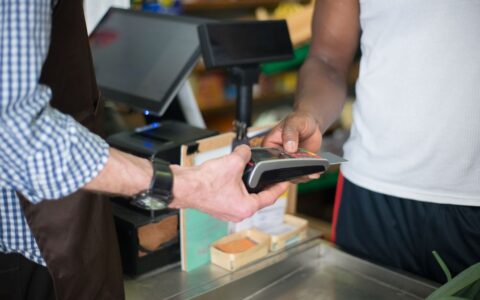 A customer making a payment with a credit card at a store checkout counter using a card reader.