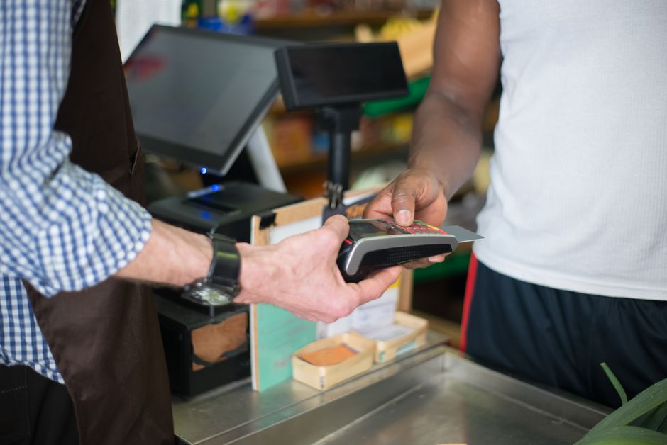 A customer making a payment with a credit card at a store checkout counter using a card reader.