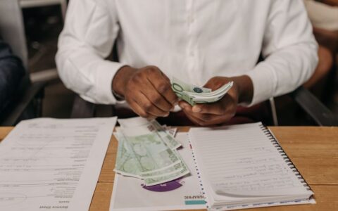 African businessman counting euro bills at a desk with documents and a notebook, highlighting finance theme.