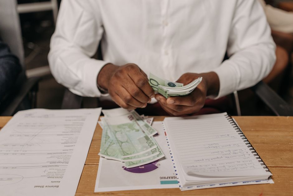 African businessman counting euro bills at a desk with documents and a notebook, highlighting finance theme.