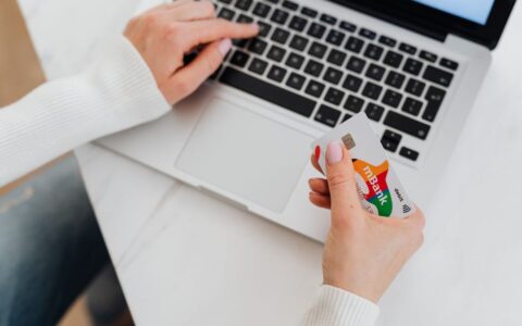 Close-up of a person using a laptop and holding a credit card for online shopping.