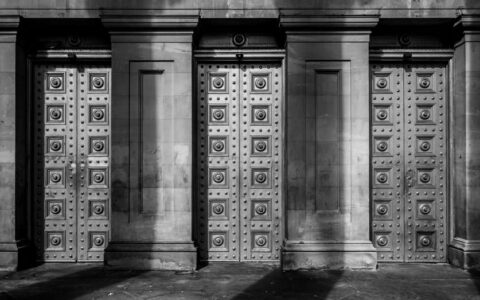 Black and white photo of an ornate architectural facade with symmetrical columns and detailed doors.