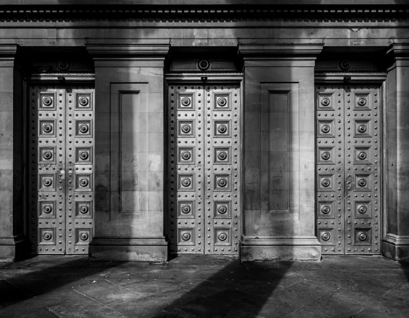 Black and white photo of an ornate architectural facade with symmetrical columns and detailed doors.