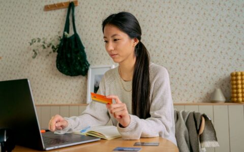 Young Asian woman using a laptop and credit card for online shopping at home.