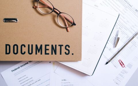 Flat lay of office supplies including documents, calendar, and eyeglasses on a desk.