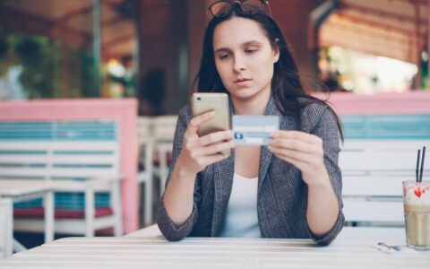 Woman using smartphone for online shopping at a cafe with credit card in hand.