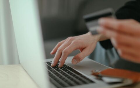 Close-up of hands holding a credit card and typing on a laptop keyboard for online shopping.