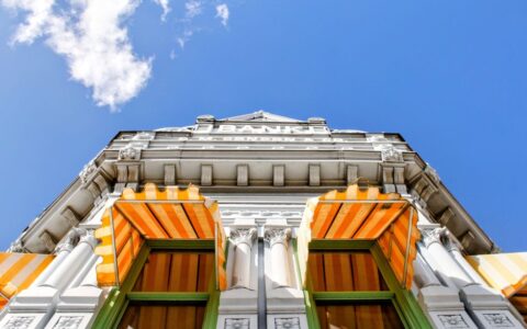Upward view of a historic bank facade with striped awnings under a vibrant blue sky in Coffeyville, KS.