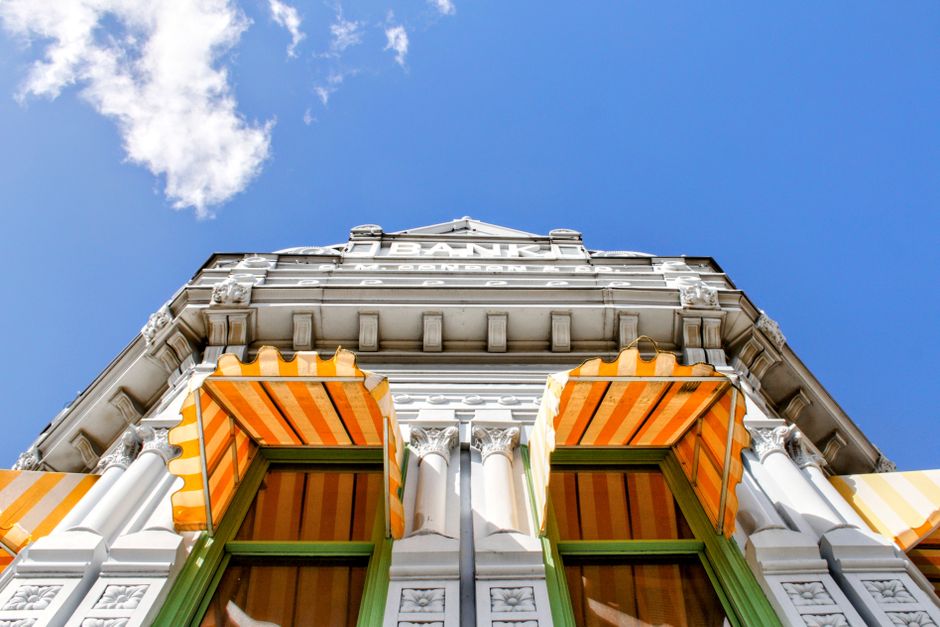 Upward view of a historic bank facade with striped awnings under a vibrant blue sky in Coffeyville, KS.