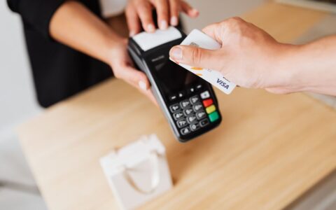 Close-up of hands using a contactless payment terminal with a credit card indoors.