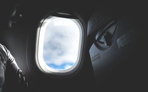Silhouette of a passenger looking through an airplane window at the clouds outside.