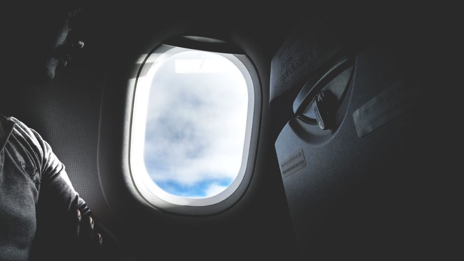 Silhouette of a passenger looking through an airplane window at the clouds outside.