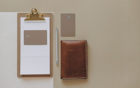 Flat lay of a minimalist office desk with clipboard, credit cards, pen, and leather wallet.