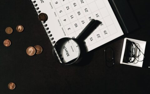 Top view of a calendar with a magnifying glass and coins, ideal for financial themes.