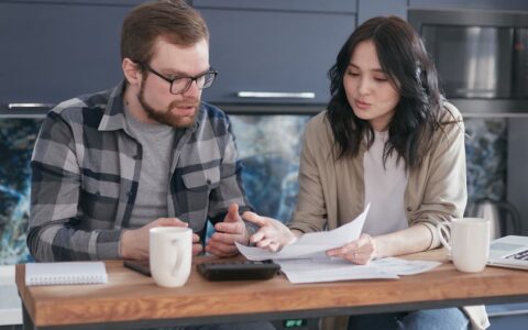 A couple having a serious discussion and reviewing documents at a kitchen table.