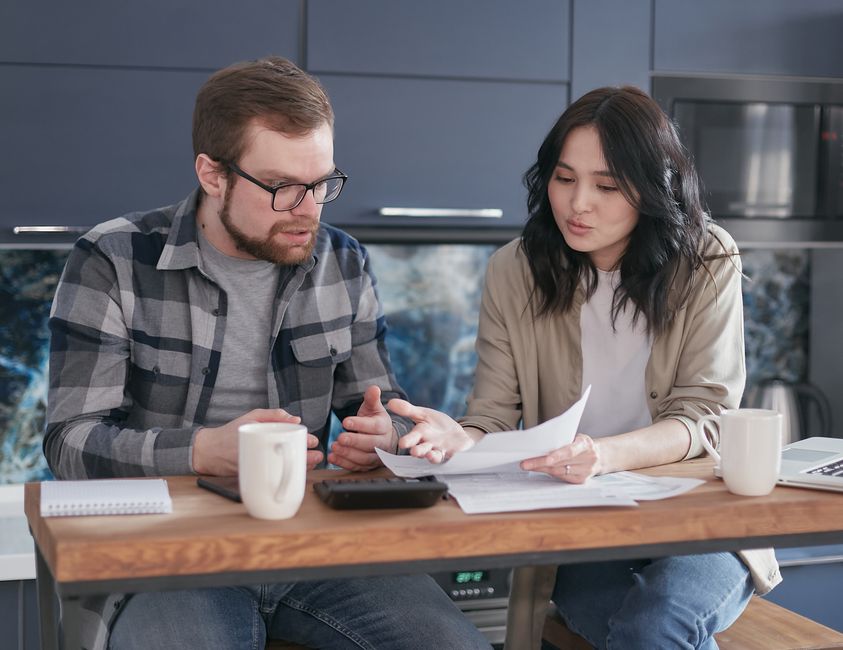 A couple having a serious discussion and reviewing documents at a kitchen table.