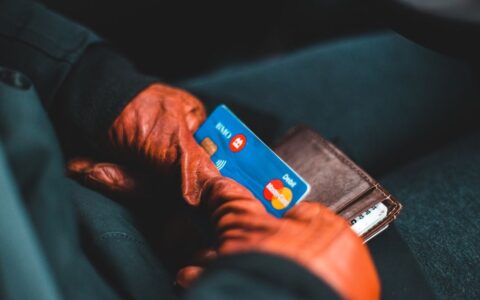 Close-up of hands in gloves holding a credit card and wallet indoors.