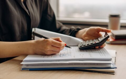 Close-up of person using a calculator with financial documents in an office.